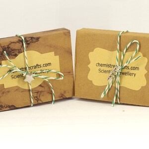 May include: Two small, brown cardboard boxes tied with twine and a green and white ribbon. The boxes have labels with the text "chemistrecrafts.com Scientific Jewellery".