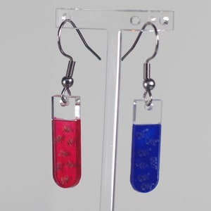 Puede incluir: Un par de pendientes colgantes con tubos de acrílico transparente rellenos de resina roja y azul. La resina tiene un efecto brillante.
