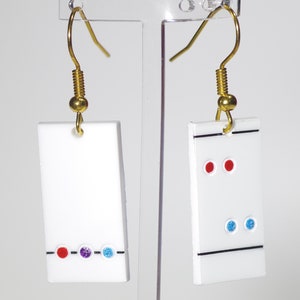 May include: A pair of white rectangular earrings with gold hooks. One earring has a black line and three dots: red, purple, and blue. The other earring has a black line and two red dots above two blue dots.