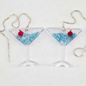 May include: A pair of silver chain earrings with a clear glass martini glass charm filled with blue glitter and a red cherry.