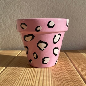 Può includere: Un vaso di terracotta rosa con un design a stampa animalier in bianco e nero.