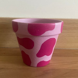 Könnte beinhalten: Ein rosa Terrakotta-Pflanztopf mit Kuhmuster. Der Topf hat rosa und magentafarbene Flecken.