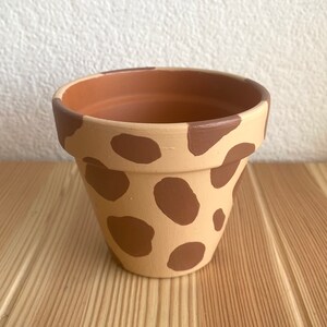 May include: A terracotta flower pot with a brown and beige giraffe print.