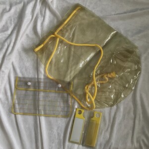 May include: A collection of clear, yellow-trimmed travel accessories, including a drawstring bag, a small pouch with snap closures, and two yellow combs. The items are arranged on a white, textured surface.