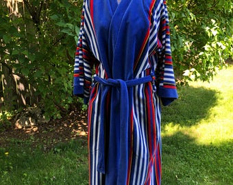 May include: A blue robe with vertical stripes in red, white, and yellow. The robe has a matching belt and is displayed on a mannequin. The robe's sleeves and collar are trimmed with red and yellow stripes.