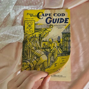 Peut inclure: Un numéro vintage du magazine Your Weekly Cape Cod Guide daté du 21 juillet 1973. La couverture jaune présente des illustrations à l'encre noire de personnes sur un quai, un navire et des tonneaux. Le texte inclut "Cape Cod Guide" et "Mail Back Home".