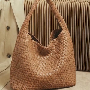 May include: A woven brown shoulder bag with a large, open design. The bag features a braided handle and a textured, basket-weave pattern. The bag is made of a soft, flexible material and is suitable for everyday use.