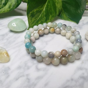 May include: A double-strand bracelet made of light green, blue, and white gemstone beads. The bracelet is on a white marble surface.