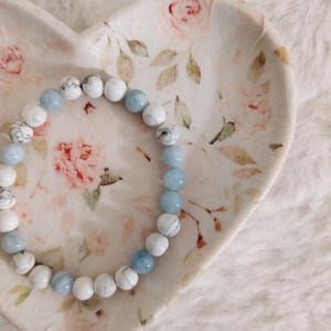 May include: A circular beaded bracelet featuring alternating smooth light blue beads and white beads with grey veining. The bracelet is arranged in a circular pattern, showcasing a mix of solid-colored and marbled stone-like spherical beads.