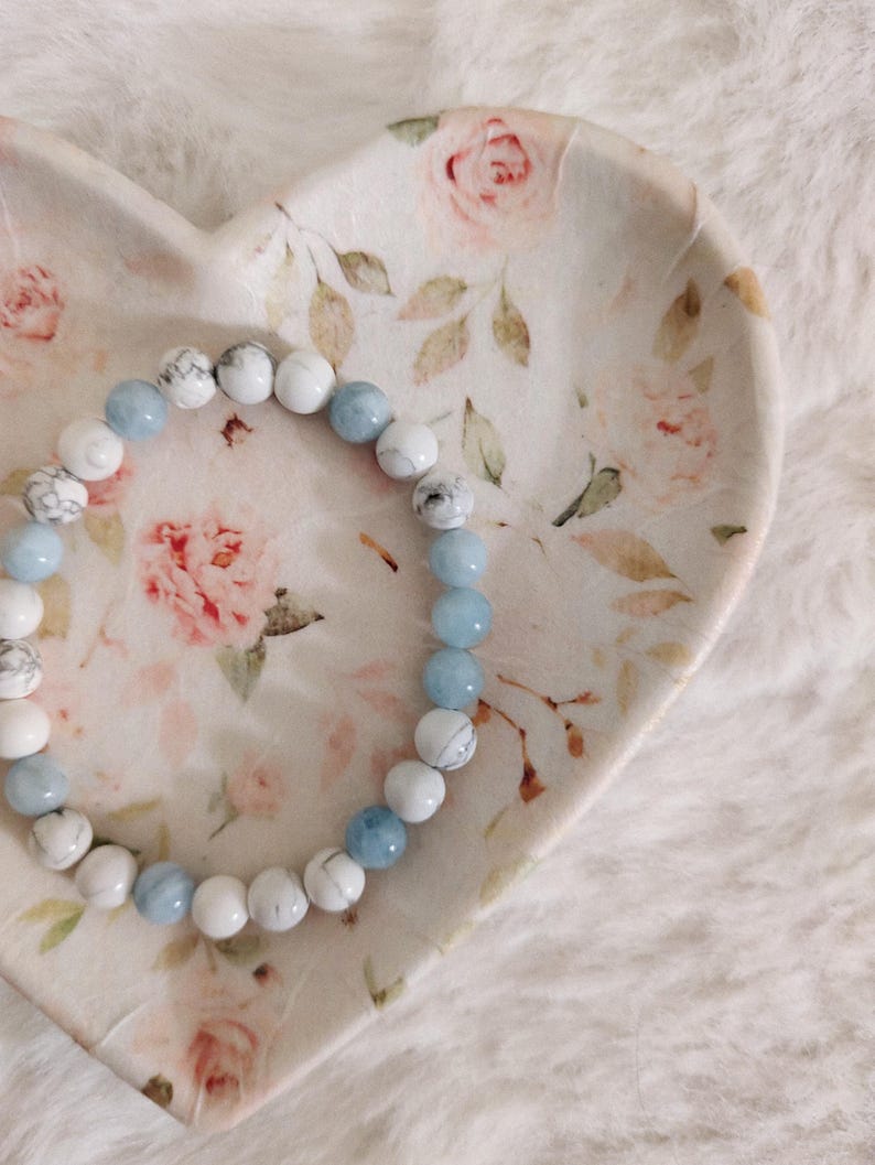 May include: A circular beaded bracelet featuring alternating smooth light blue beads and white beads with grey veining. The bracelet is arranged in a circular pattern, showcasing a mix of solid-colored and marbled stone-like spherical beads.