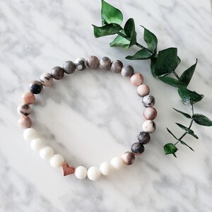 May include: A bracelet made of white and pink marbled beads with a rose gold heart charm.
