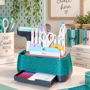 May include: A teal glittery desktop organizer with a pull-out drawer containing various pens. The organizer holds multiple Cricut brand crafting tools, including scissors, scrapers, and weeding pens, arranged in dedicated slots on the top surface.