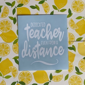 May include: A light blue vinyl decal with white lettering that reads "Dedicated teacher even from a distance". The decal is on a white background with a pattern of yellow lemons.