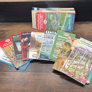 Peut inclure: Une collection de guides et de cartes de voyage vintage, présentant diverses destinations. Les guides ont des couvertures colorées avec du texte et des illustrations. Certains titres incluent "Atlantic Provinces", "Québec" et "Extended Tours from London."
