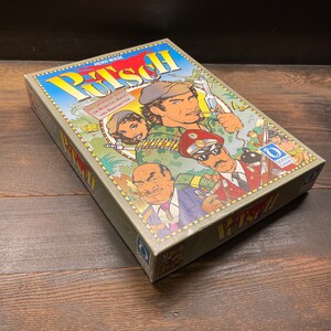 May include: A board game box titled "Putsch" with illustrations of military figures and the text "Das satirische Spiel um Moneten, Macht und Marionetten." The box is olive green with a colorful illustration and the Queen Games logo.