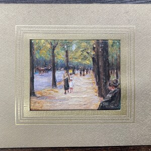 May include: An impressionistic painting of a tree-lined street scene, featuring figures strolling along a path. The artwork is framed in a gold-toned mat, enhancing the vintage aesthetic. The painting captures a moment in time with soft colors and brushstrokes.
