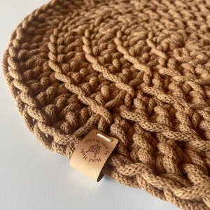 Könnte beinhalten: Ein runder brauner Häkeluntersetzer mit einem Lederanhänger, auf dem "Hand Made by Inner Stitches" steht.
