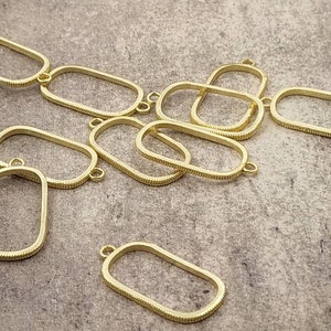 Puede incluir: Una colección de hallazgos de joyería ovalados y rectangulares dorados de marco abierto. Cada pieza tiene un borde texturizado y pequeños bucles para conectar a otros componentes. Estos hallazgos son ideales para crear collares, pulseras y aretes.