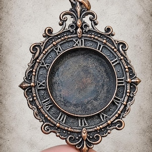 May include: A circular pendant featuring a dark, recessed center surrounded by a raised border with Roman numerals. The frame is crafted from a metallic material with a copper-toned finish and intricate, ornate scrollwork detailing.