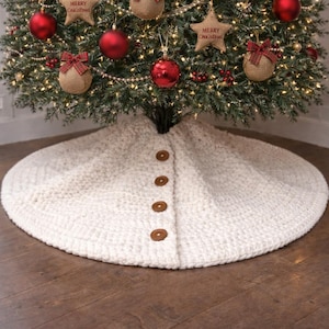 Könnte beinhalten: Ein geschmückter Weihnachtsbaum mit roten Kugeln, Schleifen aus Jute und sternförmigen Ornamenten mit der Aufschrift "Merry Christmas". Der Baum steht auf einem cremefarbenen Baumrock mit Knöpfen auf einem Holzboden.