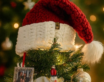 May include: A decorated Christmas tree with a red and white Santa hat as a tree topper. The tree is adorned with various ornaments, including a framed photo, a nutcracker, and several baubles. The overall theme is festive and holiday-oriented.