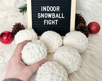 May include: Six white crocheted snowballs on a white fluffy surface with a black letter board that says "Indoor Snowball Fight".