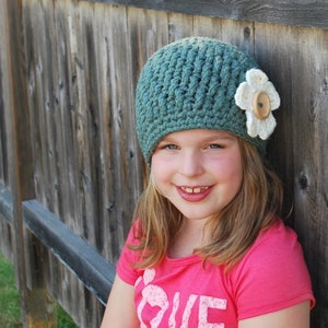 May include: A young girl wearing a teal blue crocheted hat with a white flower and a pink shirt that says "LOVE" on it.