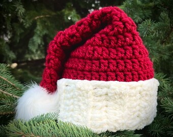 May include: A red and white crocheted Santa hat with a white pom-pom. The hat is made with a soft, fluffy yarn.