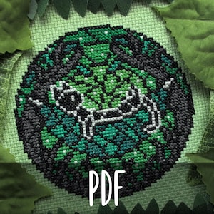 Pode incluir: Um padrão de ponto cruz com um design estilizado de gato em tons de verde e preto, rodeado por uma borda de folhas. A palavra "PDF" é exibida em texto branco na parte inferior. O design é circular e está sobre um fundo verde claro.