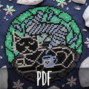 Può includere: Schema a punto croce con un disegno di gatto nero con una tazza blu, circondato da un bordo verde. Il disegno è circolare, con la parola "PDF" in bianco in basso. Fiocchi di neve decorativi e forme bianche sparse.