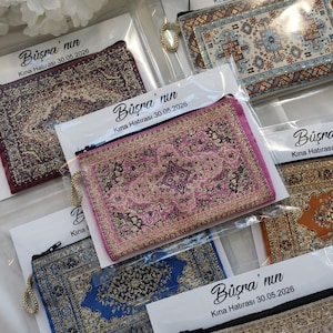 May include: Small, rectangular fabric pouches with detailed carpet-style designs in shades of pink, blue, and gold. Each pouch features a zip closure and a gold-coloured wrist strap. The pouches are packaged with a label that includes text.