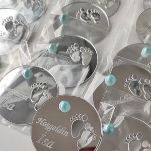 May include: Silver round mirror with a blue gem in the centre. The mirror has a design of two baby footprints and the text "Hosgeldin Isa".