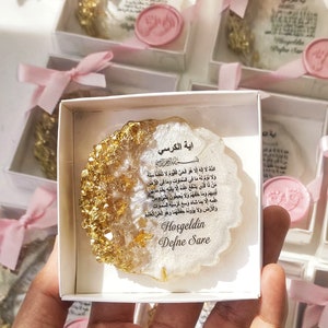 May include: A white box with a pink ribbon contains a white and gold resin ornament with Arabic text and the words "Hoşgeldin Defne Sare".