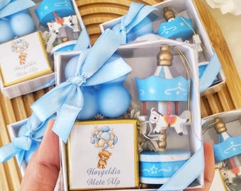 May include: Blue and white favour boxes with a carousel, balloons, and a teddy bear holding balloons. The boxes have a tag that says "Hosgeldin Mete Alp".