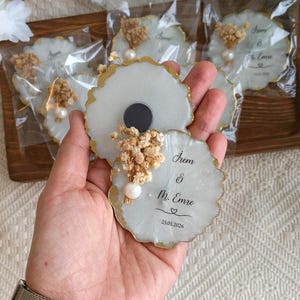 May include: White and gold-edged resin magnets with dried floral accents and a pearl. Each magnet has the names "Irem & Mr. Emre" and the date "25.01.2026" printed on it. The magnets are packaged in clear plastic.