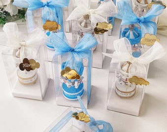 May include: Blue and white carousel favours in clear boxes tied with blue and white ribbon. Each box has a gold tag with the name "Huseyin" on it.
