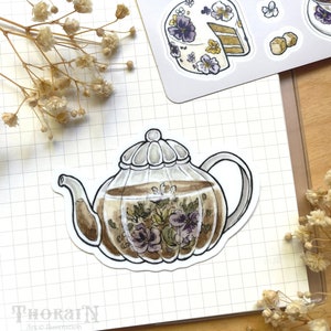 May include: A sticker of a glass teapot with a floral design. The teapot is filled with brown tea and has a clear lid. The sticker is on a white gridded background.