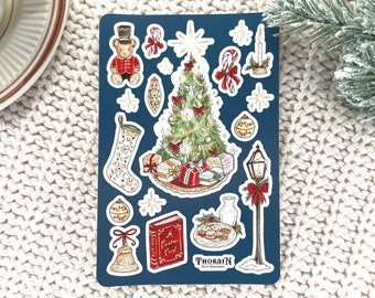 Può includere: Un foglio di carta blu con una varietà di adesivi a tema natalizio. Gli adesivi includono un albero di Natale, una calza, un libro, una campana, una canna di zucchero, una stella, un lampione, un orso e un piatto di biscotti. Gli adesivi sono tutti disegnati a mano e hanno un aspetto vintage.