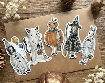 May include: Five Halloween-themed stickers featuring a ghost, a pumpkin, a witch, a bunny, and a clown. The stickers are on a brown background.