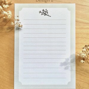 May include: A white lined stationery sheet with a light green border and a small floral illustration in the top center. The text "Design 2" is at the top of the sheet and the text "THORAIN art & illustration" is at the bottom of the sheet.