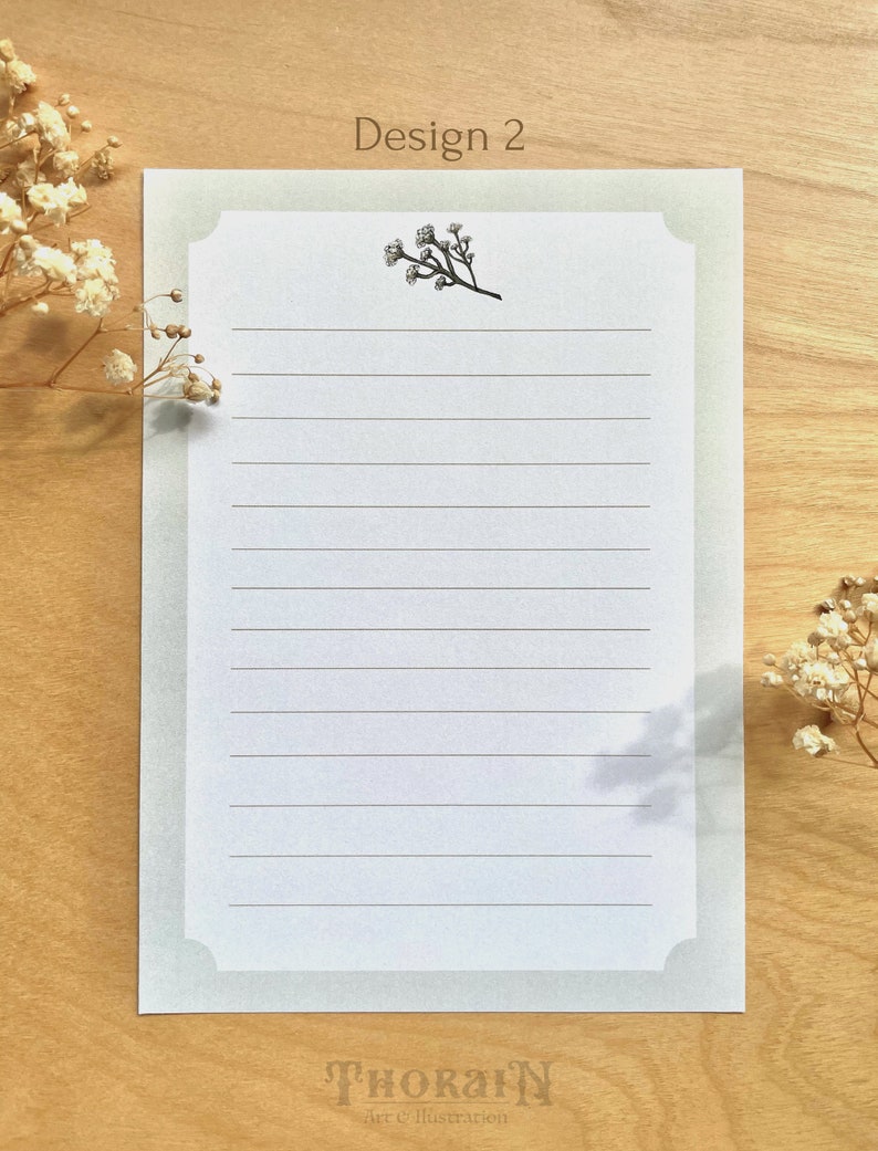 May include: A white lined stationery sheet with a light green border and a small floral illustration in the top center. The text "Design 2" is at the top of the sheet and the text "THORAIN art & illustration" is at the bottom of the sheet.