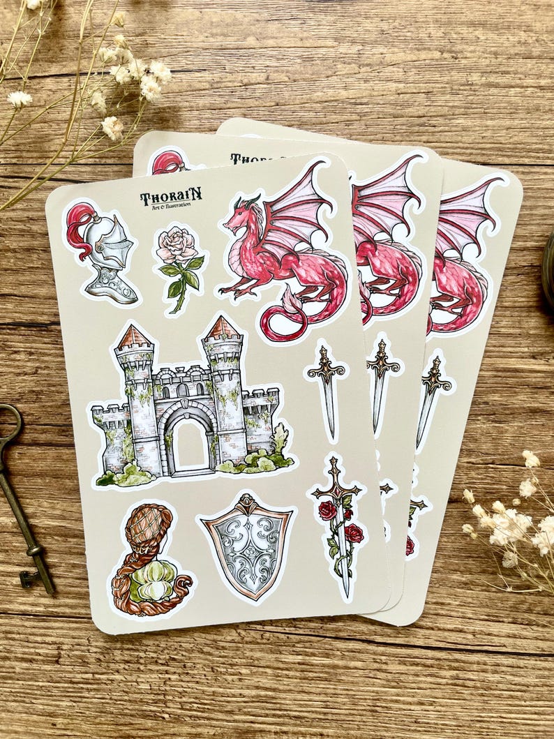 May include: Three sheets of stickers featuring a red dragon, a castle, a sword with roses, a shield, a knight's helmet, a rose, and a woman with long hair. The stickers are on a beige background and have the text "THORAIN Art & Illustration" on them.