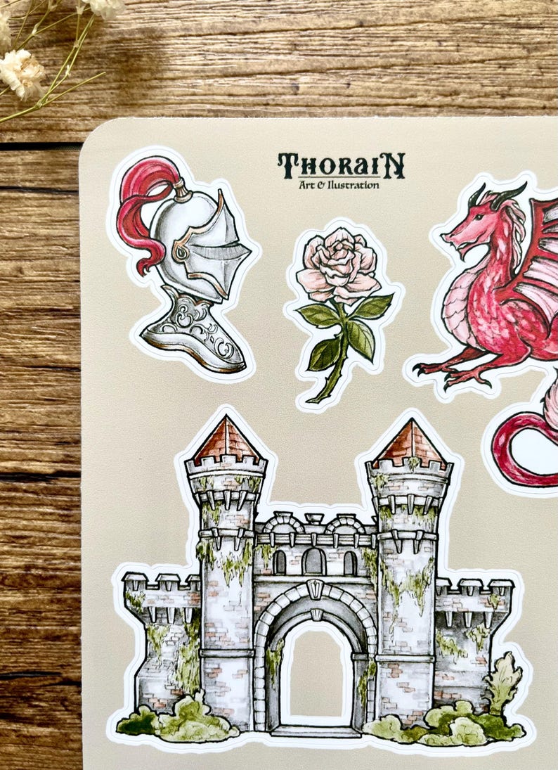 May include: A set of five stickers featuring a red dragon, a white knight's helmet with a red plume, a white rose with green leaves and stem, and a gray stone castle with a red roof and green vines. The stickers are on a beige background. The text "ThoraiN Art & Illustration" is printed in black at the top of the sheet.
