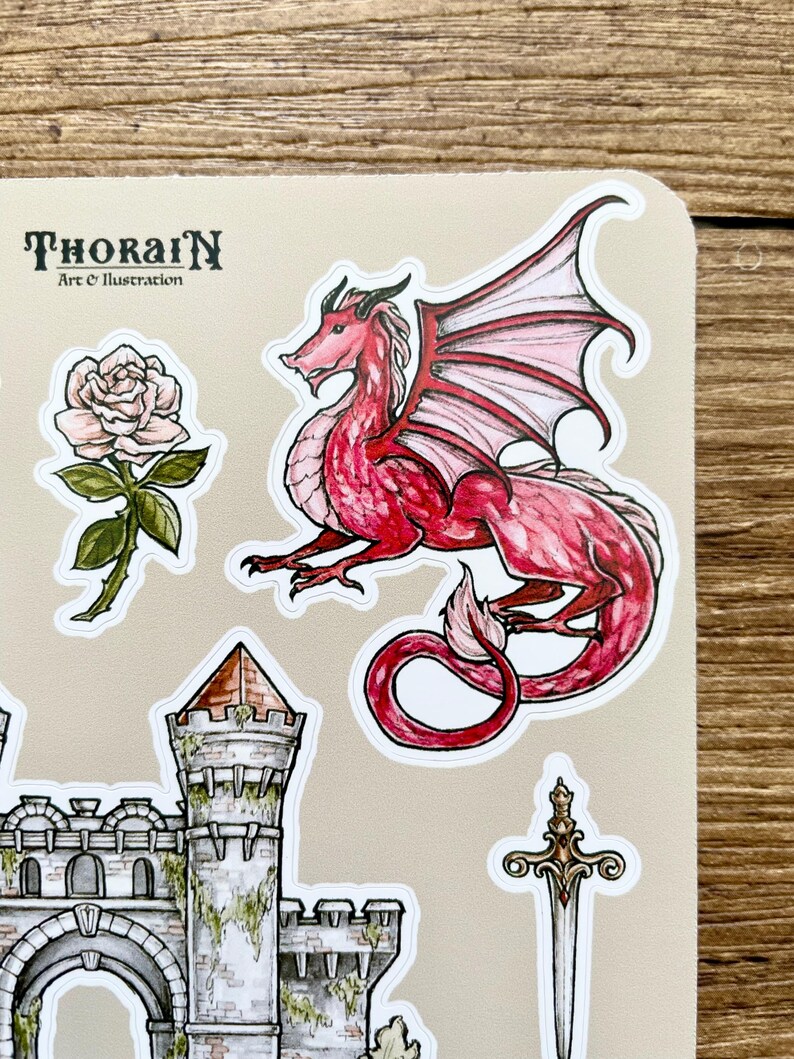 May include: A set of stickers featuring a red dragon with pink wings, a stone castle with a green ivy, a white rose with green leaves, and a silver sword with a gold handle. The stickers are on a beige background with the text "THORAIN Art & Illustration".
