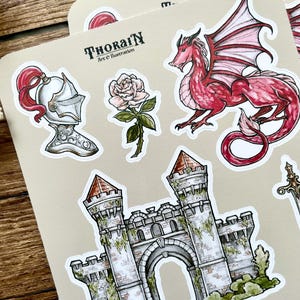 May include: A set of stickers featuring a red dragon, a white rose, a knight's helmet, a stone castle, and the text "THORAIN Art & Illustration".