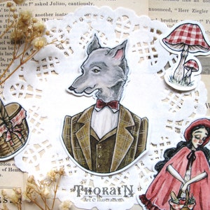 Puede incluir: Un conjunto de tres pegatinas ilustradas que representan un lobo con traje y corbata de lazo, una niña con capucha roja que lleva una cesta y un hongo de cuadros rojos y blancos. Las pegatinas están sobre una servilleta de encaje blanca con un patrón floral.