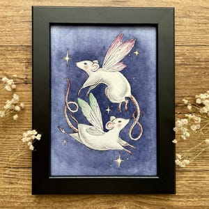 May include: A framed art print featuring two white mice with fairy wings, set against a dark blue background with stars. The mice are depicted in flight, with one having pink wings and the other green. The frame is black.