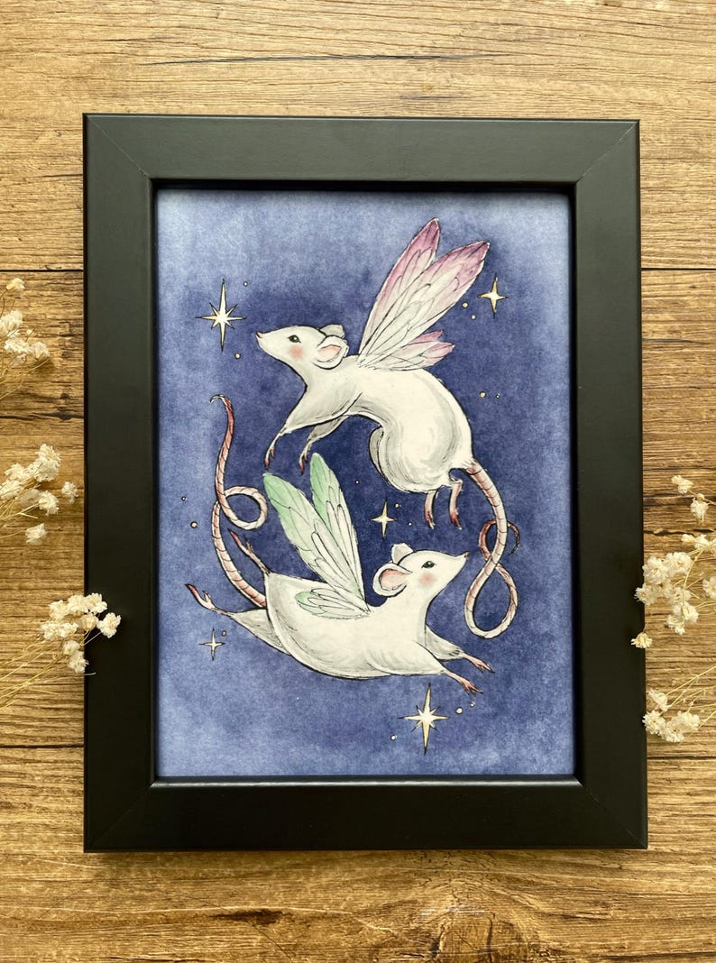 May include: A framed art print featuring two white mice with fairy wings, set against a blue background with stars. The mice are depicted in mid-flight, with one pair of wings in pink and the other in green. The artwork is enclosed in a black frame.