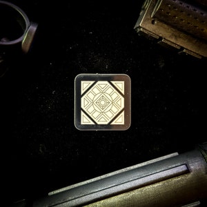 May include: A white and gray geometric design on a square metal tile. The design features a central circle with four radiating lines and a square frame.