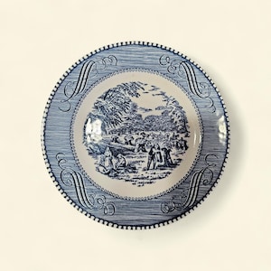 May include: A blue and white decorative plate with a detailed landscape scene in the center. The plate has a textured border and ornate scrollwork. The rim features a series of small, evenly spaced dots. The overall design is classic and elegant.
